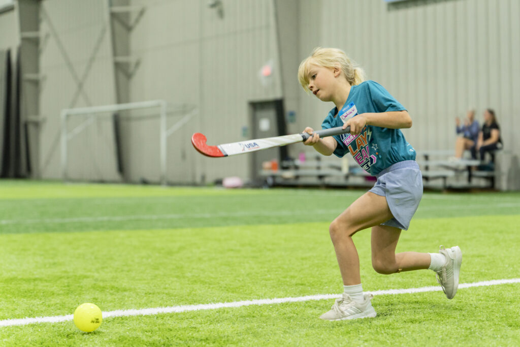 Young girl swinging at a ball while playing field hockey.