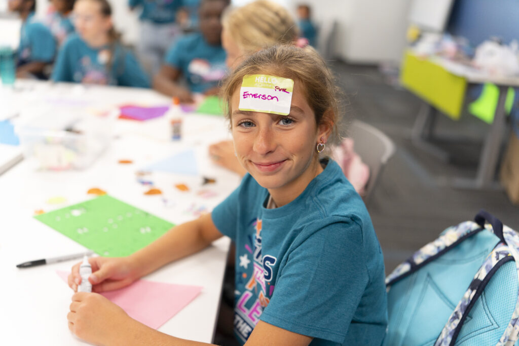 Young girl smiling at camera with sticker on her forehead.