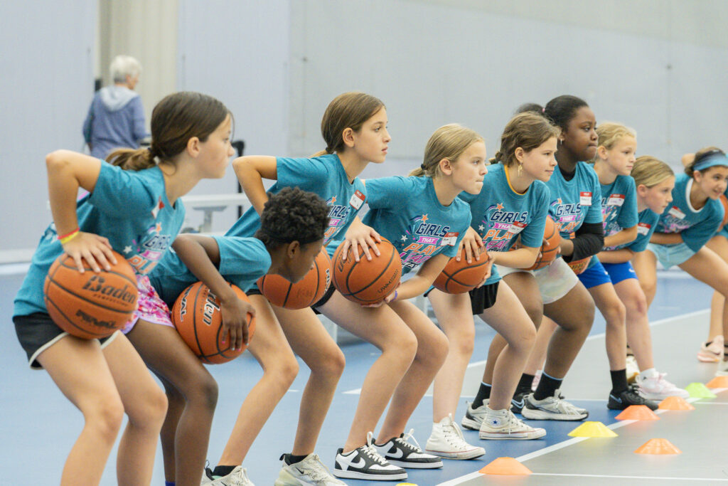 Young girls hunched in a line performing basketball drills.